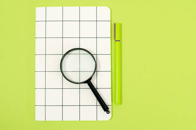 Flat lay of notebook, magnifying glass, and pen on a green background, perfect for office themes. Business licences benchmark research: a method